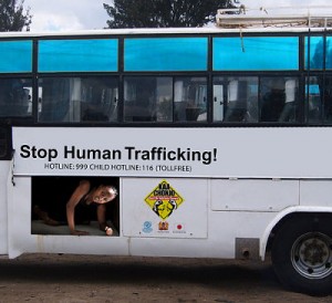 ID: Image of an advertisement on the side of a bus that has an image of a person crouched on the floor in distress and the words Stop Human Trafficking
