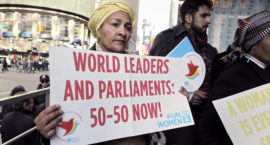 a woman holds a sign reading WORLD LEADERS AND PARLIAMENTS: 50-50 NOW!