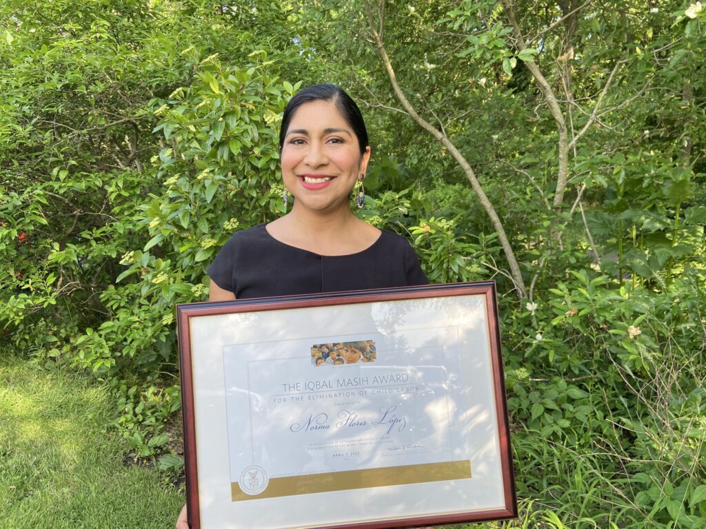 Norma Flores López standing with Iqbal Masih Award, awarded to her in 2021 for her work in child labor rights.