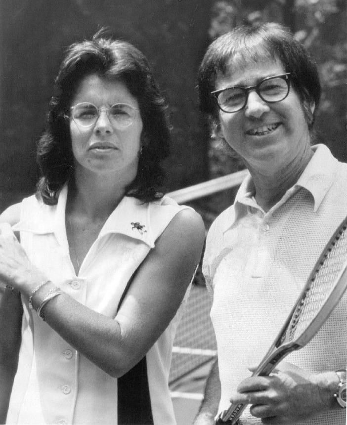 Image of Billie Jean King standing next to Bobby Riggs on a tennis court. 