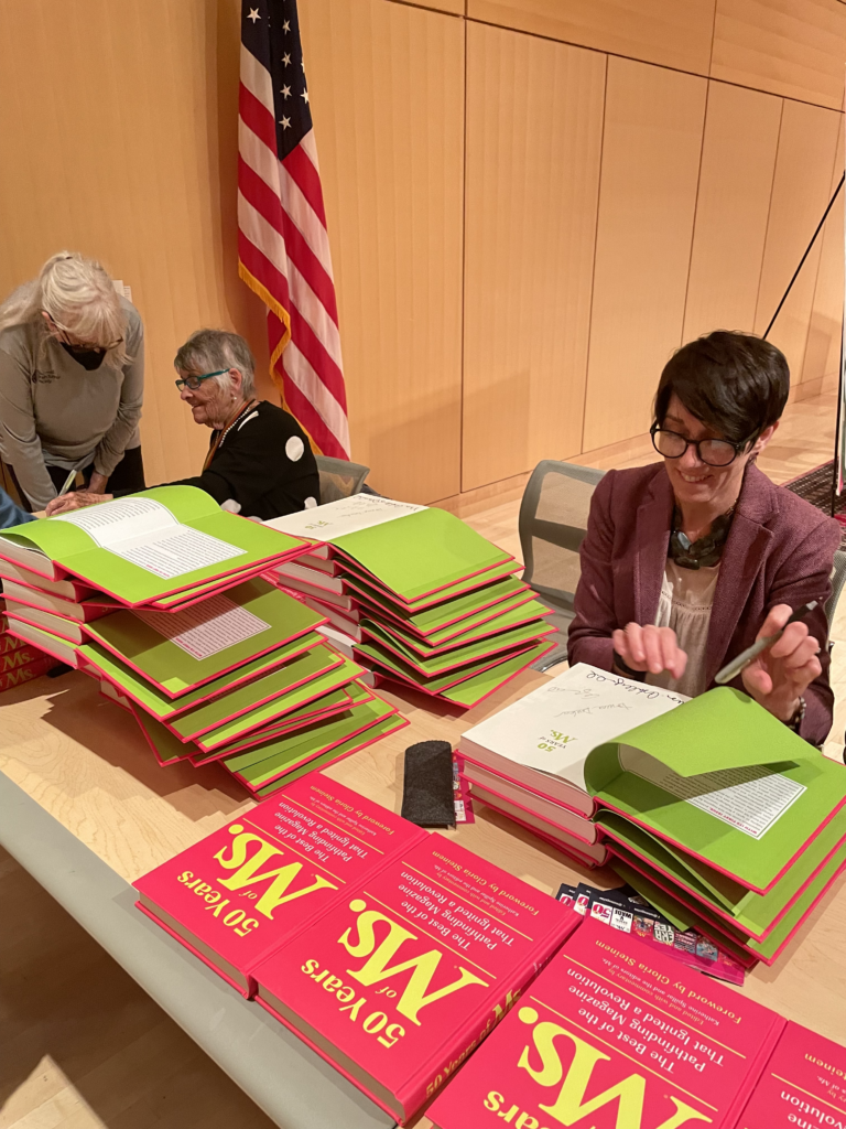 Copies of 50 Years of Ms. move down the signing line at Cambridge Public Library.