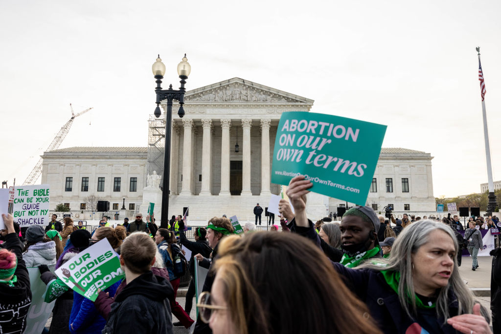 A rally outside the Supreme Court in support of abortion pills; one sign says "Abortion on our own terms"