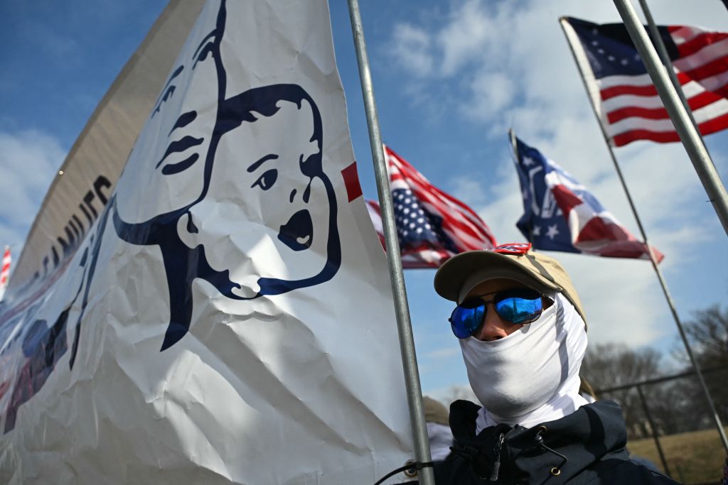 A neo-Nazi attends the March for Life wearing a white mask and holding a flag with a cartoon baby 