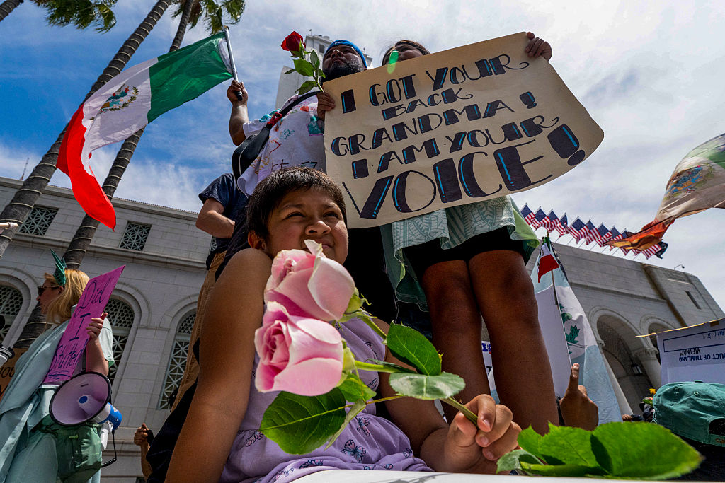 A protestor holds a sign that says, "I got your back Grandma! I am your voice!" while another protestor holds a Mexican flag.