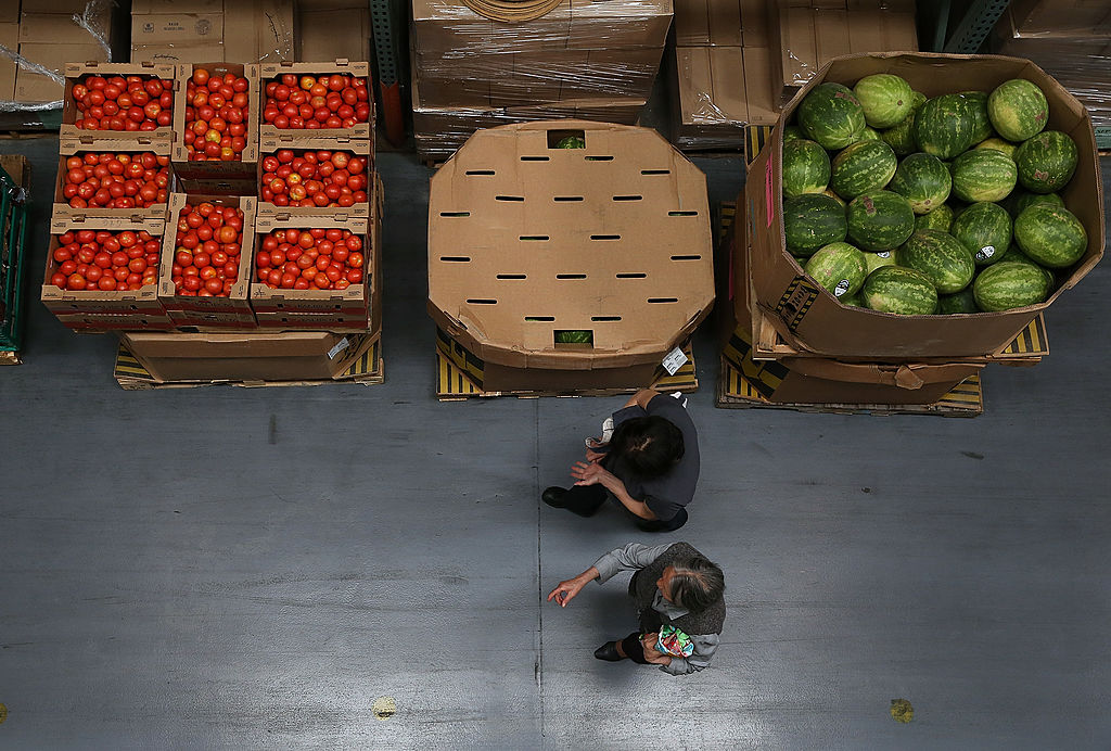 Volunteers walk by boxes of tomatoes and watermelons