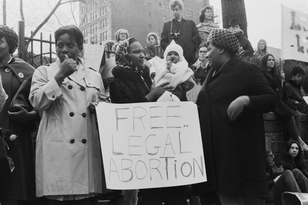 Protestors, one holding a child, stand around a placard reading 'Free legal abortion' 