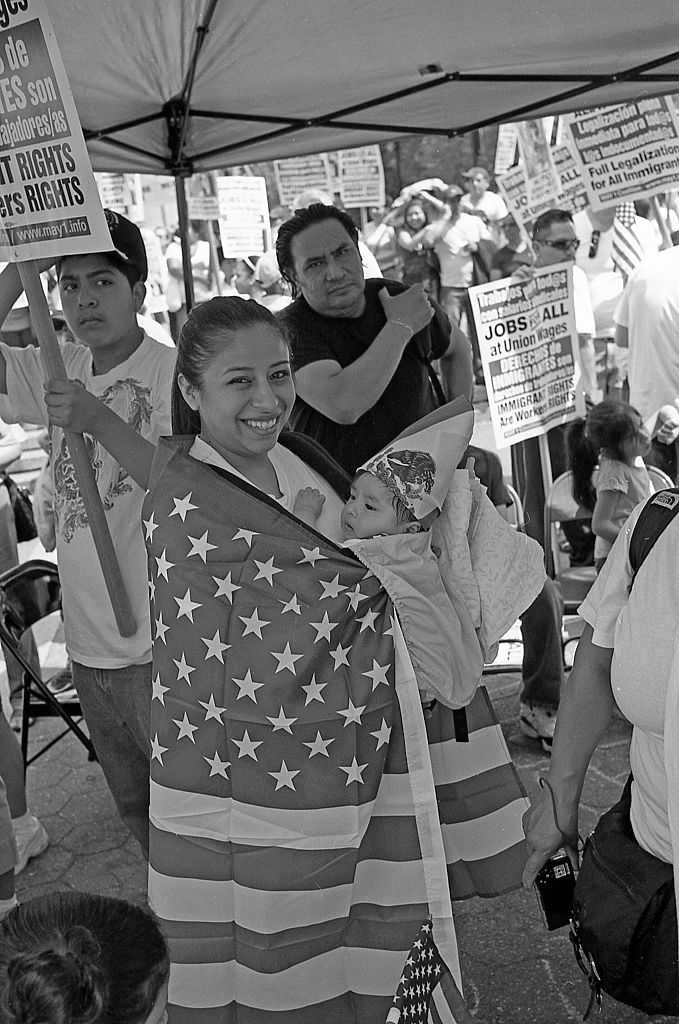 View of a demonstrator, with an American flag over her shoulders and carrying a baby, as she smiles during a 