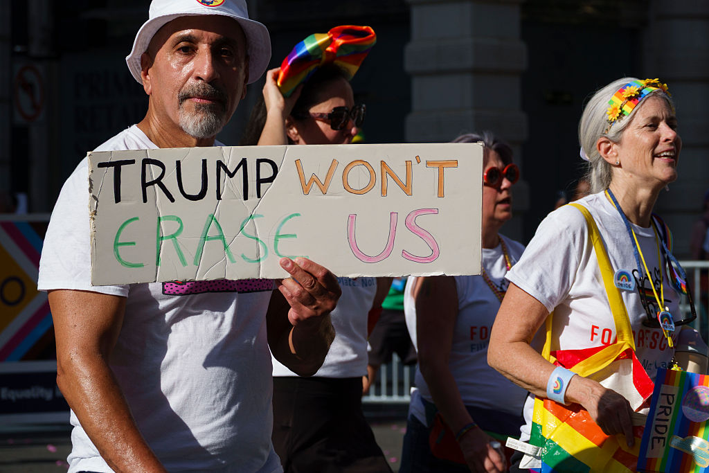 A man marching in the World Pride Parade holds up a sign that says "TRUMP WON'T ERASE US." 
