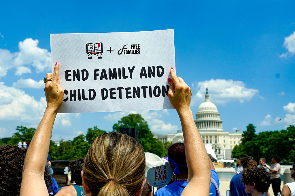 A woman with brown hair holds a sign that says "END FAMILY AND CHILD DETENTION" at a demonstration in front of the US capitol building. 
