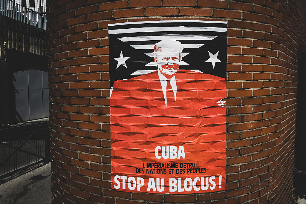 A red and navy poster denouncing Trump's attacks on Cuba is tacked on a curved brick wall.