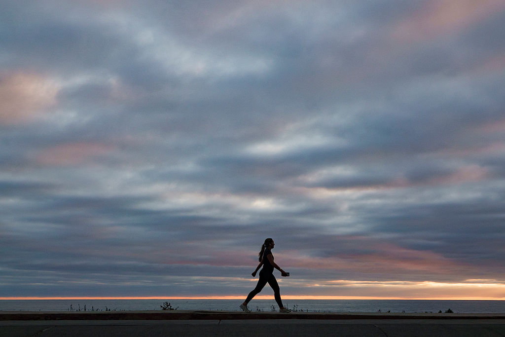 A woman carrying a mobile phone walks along the La Jolla coastline at sunset. 