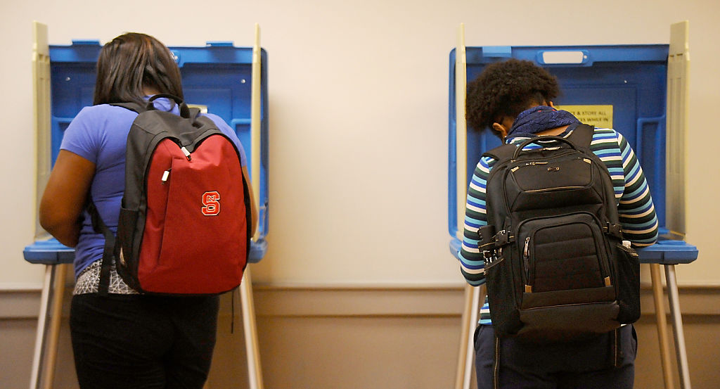 Two students are photographed from behind voting in blue voting booths. 