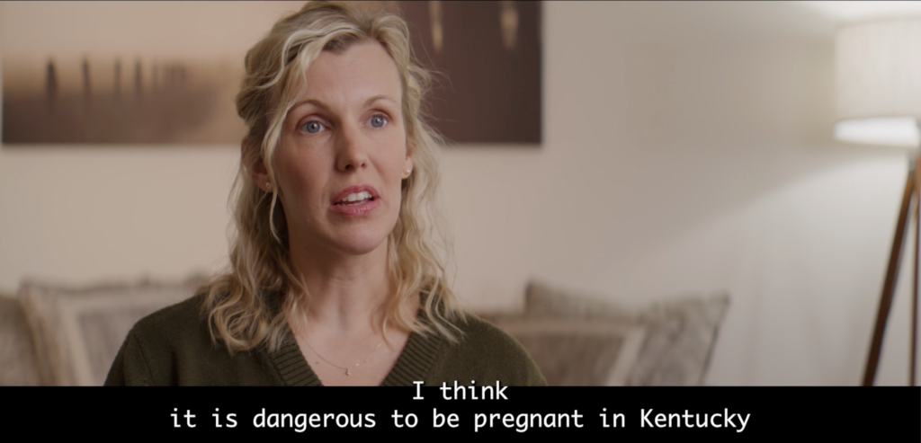 A woman with blond hair wearing a brown sweater sits in front of a beige wall during an interview about the dangers of having an abortion in Kentucky.