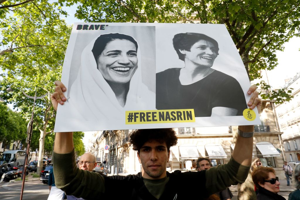 A demonstrator holds up a sign with pictures of Nasrin Sotoudeh that says "#FREENASRIN."