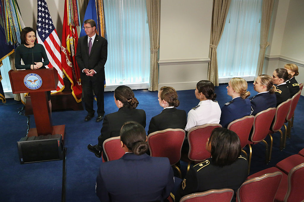 Sheryl Sandberg stands at a podium in a carpeted room and speaks to women in the military. 