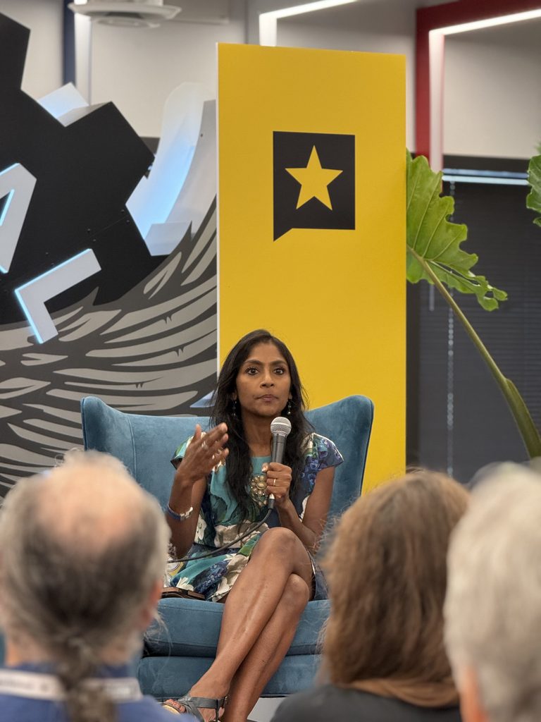 Krish O'Mara Vignarajah wears a blue and green floral dress as the speaks to an audience. 