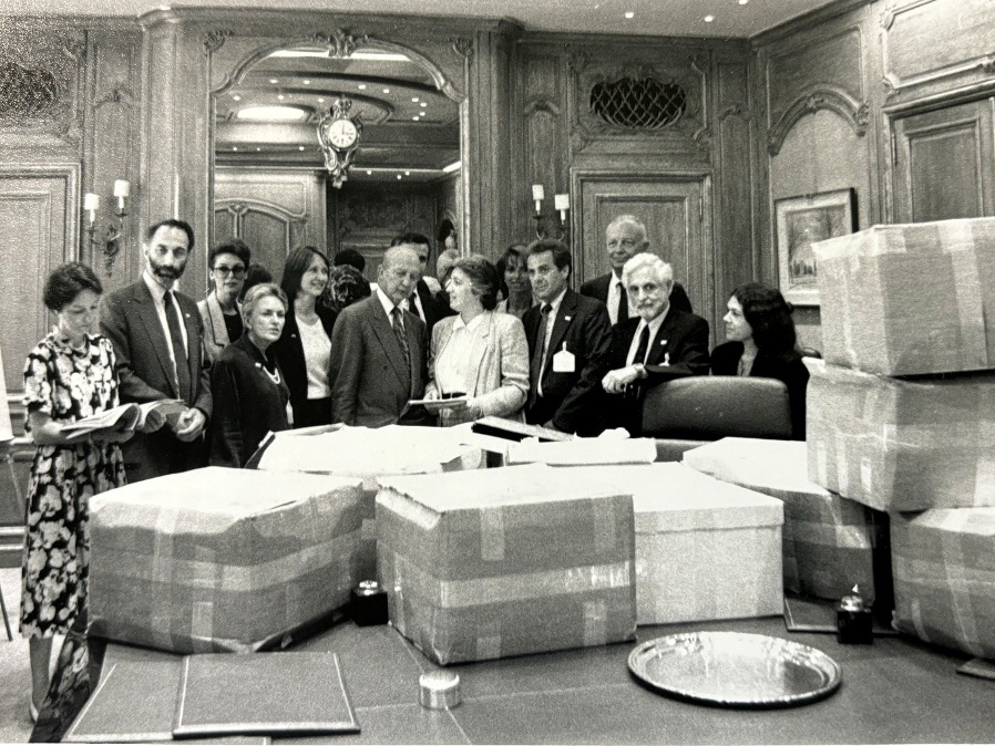 This black and white photograph shows a crowd of men and women gathered around a table of boxes.