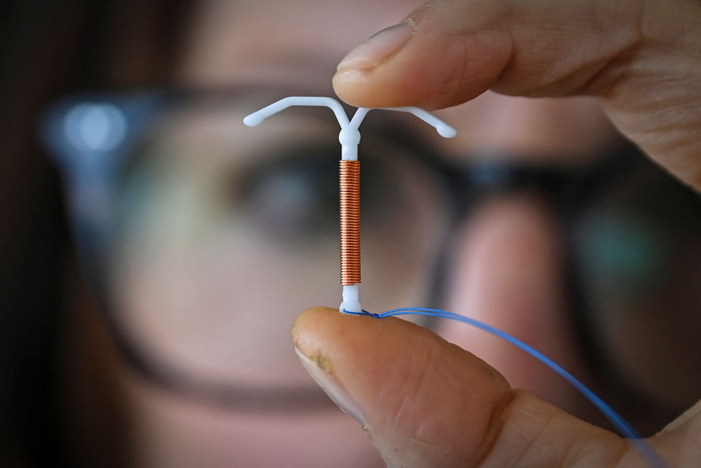 A woman with glasses holds an IUD up in front of the camera. 